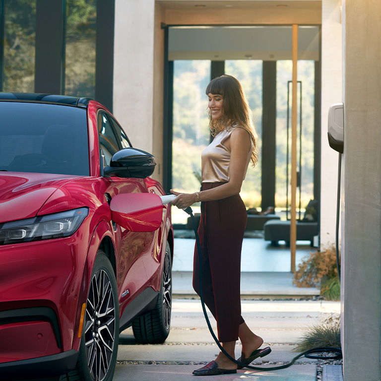 A woman connects a Mustang Mach-E to a Ford Connected Charge Station.