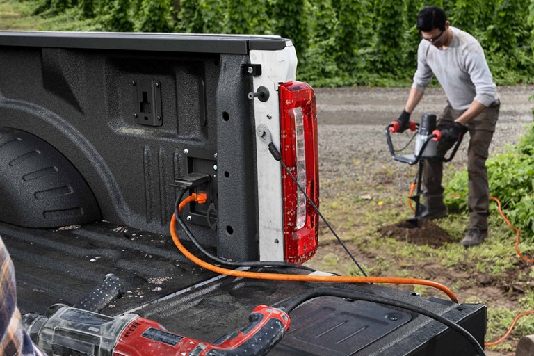 A power cord runs from the in-bed outlet to a power earth auger being used