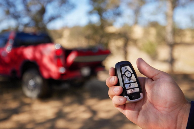 Hand holding key fob with a red 2025 Ford Super Duty® King Ranch® pickup in the background