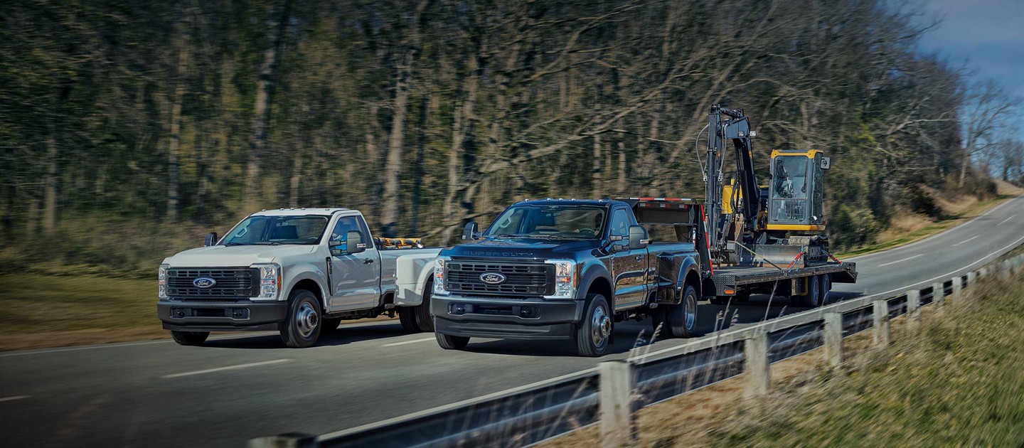 2025 Ford Super Duty® F-350® XL DRW in Oxford White and F-450® XL DRW in Antimatter Blue being driven on a paved road
