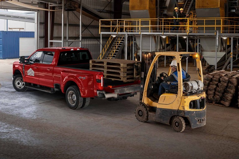 Man watching a forklift load bales of hay into the truck bed of a 2025 Ford Super Duty® F-350® LARIAT® DRW in Rapid Red