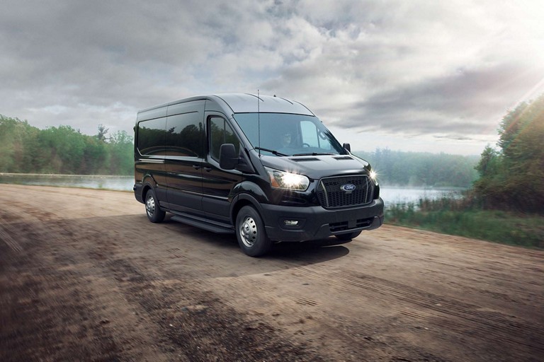 A 2025 Ford Transit® van in Agate Black with Intelligent All-Wheel Drive travels down a dirt road
