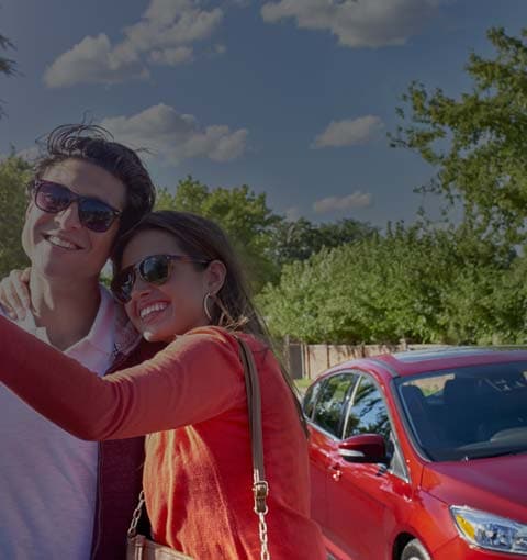 Man and woman taking a selfie with a red Ford Focus in the background