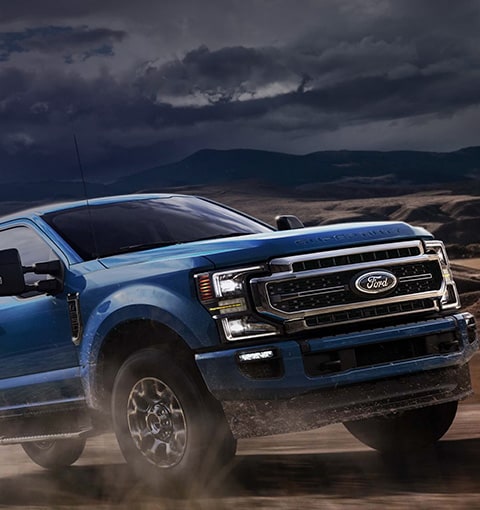 2020 Ford Super Duty in Velocity Blue being driven on dirt road with sun shining in background