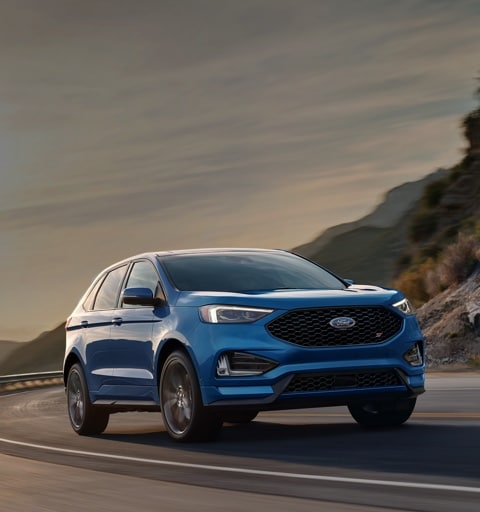 2020 Ford Edge S T in Ford Performance Blue being driven around curve on road near hills with large city in background