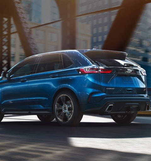 Ford Explorer with bikes on roof rack traveling road in forest