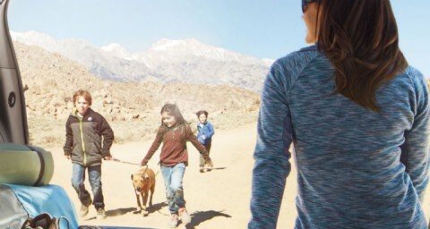 Woman sitting in open rear of a Ford Explorer while family and dog walk in desert in 