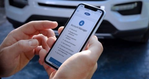 Man holding phone with Ford Credit home page, standing in front of 2020 Explorer X L