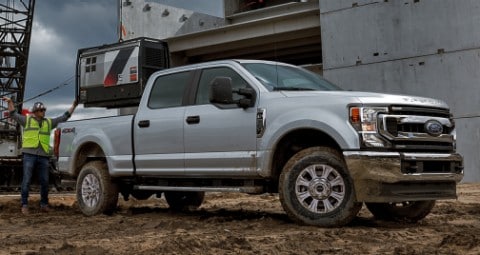 Silver Ford Truck on construction site with a worker behind the truck. 