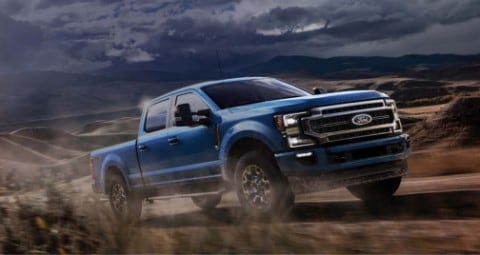 2020 Ford Super Duty in Velocity Blue being driven on dirt road with sun shining in background