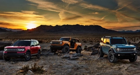 Two 2021 Ford Broncos and a 2021 Ford Bronco Sport parked in the desert with a mountain range in the background