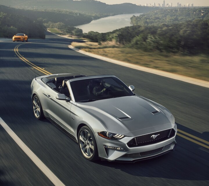 A 2021 Ford® Mustang convertible with the top down being driven on a two-lane highway