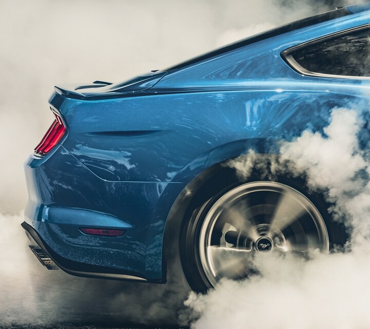 A rear wheel of a 2021 Ford® Mustang spinning to create smoke