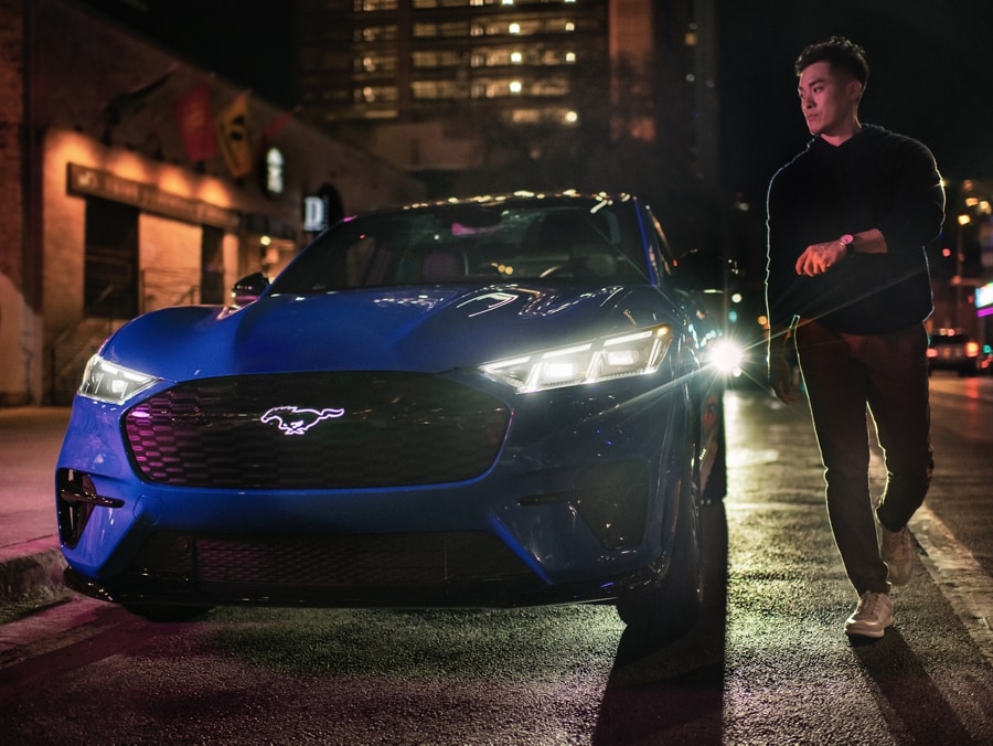 A man outside of a blue Ford Mustang Mach-E at night in the city.