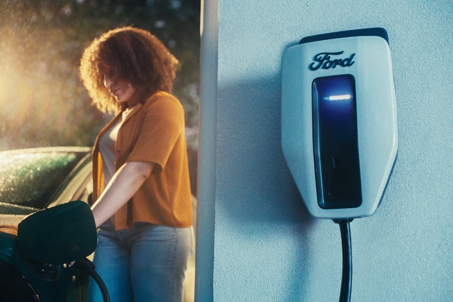 A woman charging her Mustang Mach-E in her garage with the Charge Station Pro in the foreground.