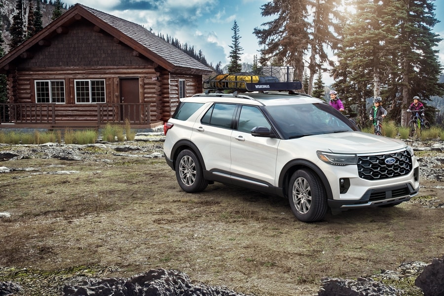 White 2025 Ford Explorer® parked outside a rustic cabin as a family on bikes approaches
