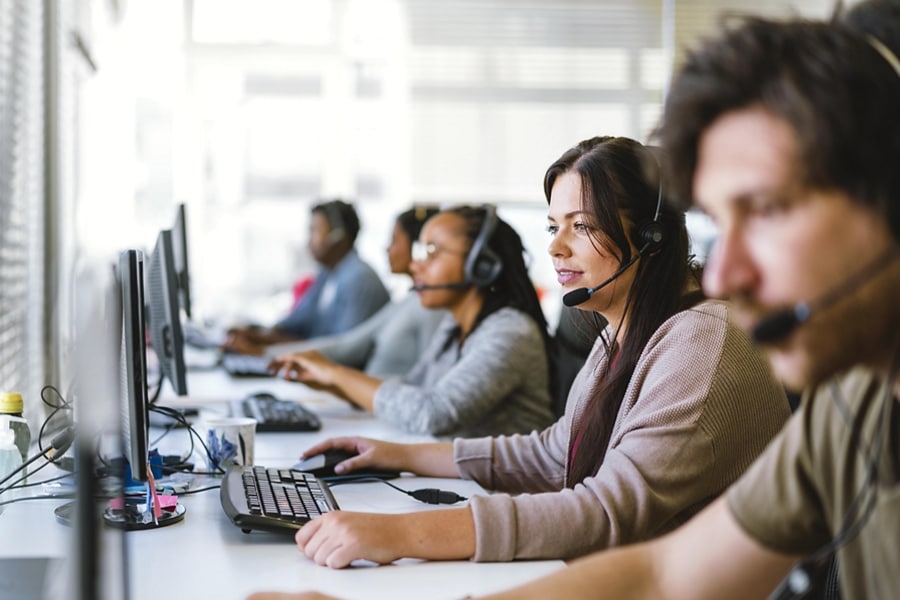 A team of customer service agents, all wearing headsets, seated at a row of computers