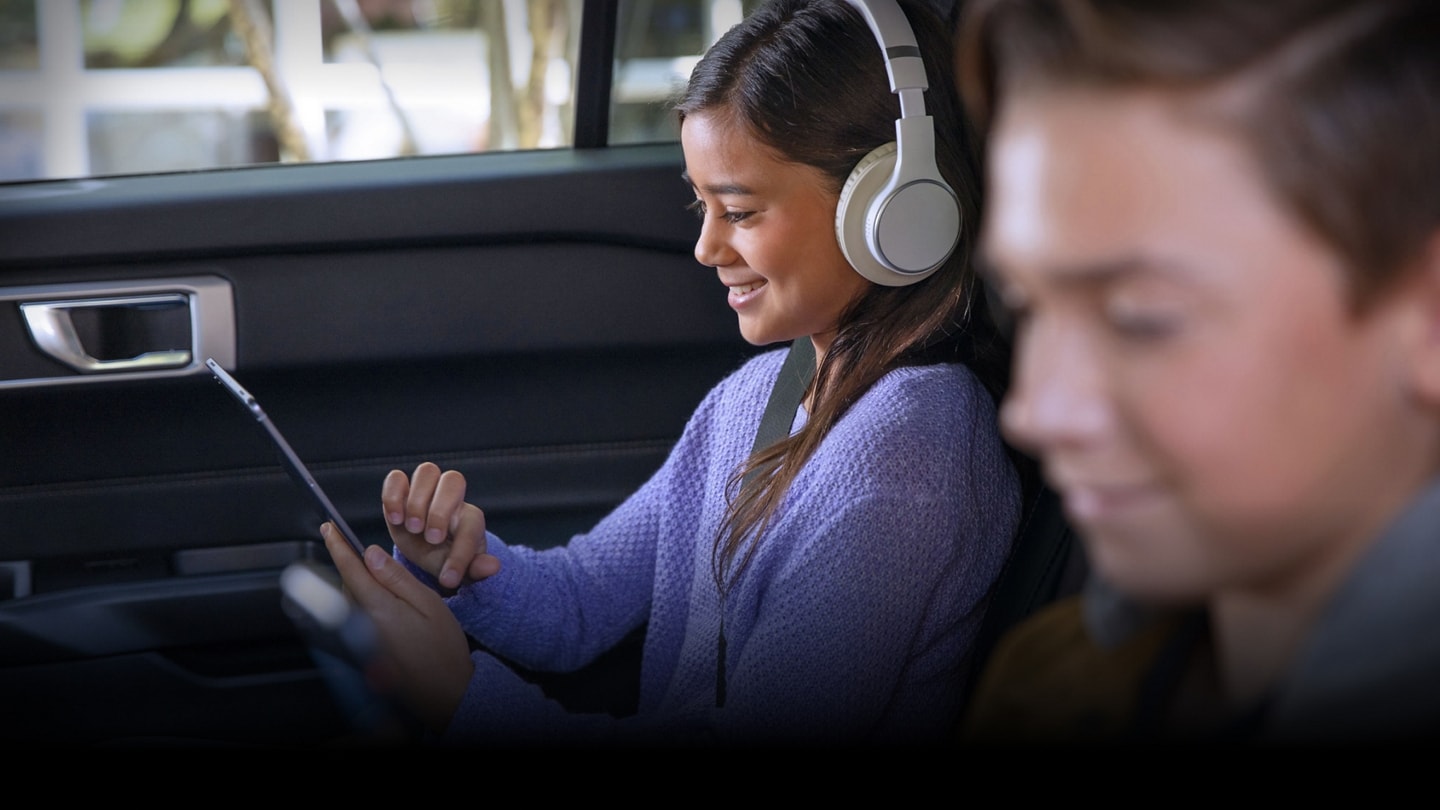 Two smiling children using mobile devices while sitting in the second and third rows of a Ford SUV.