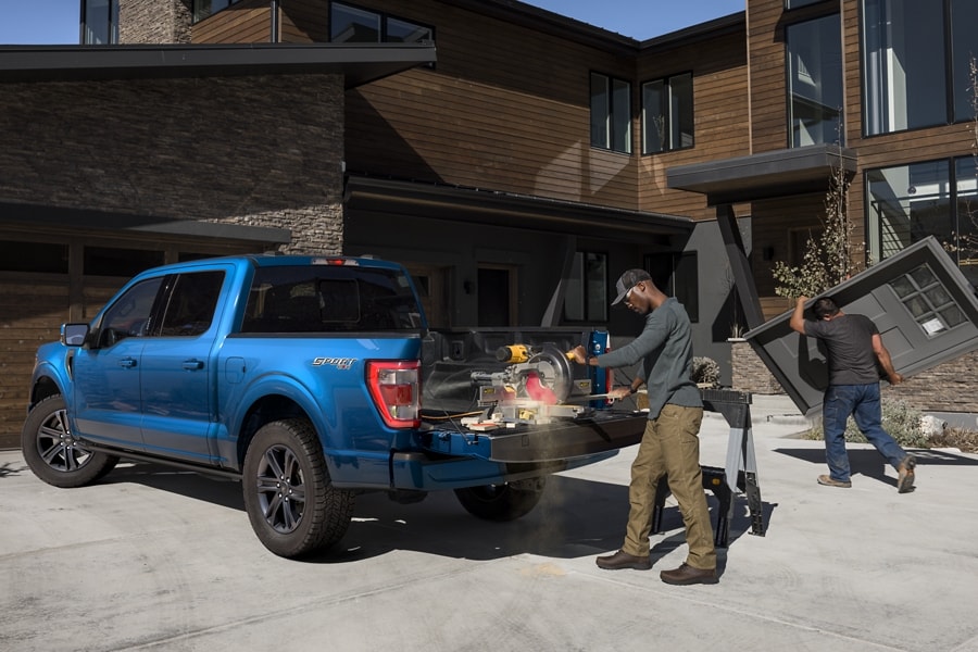 Man cutting wood with a power saw on the tailgate of a 2022 Ford F-150® LARIAT SuperCrew® in Atlas Blue in front of a home