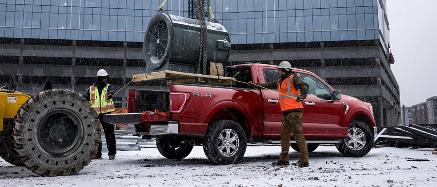 Construction workers loading a large turbine motor into the bed of a 2022 Ford F-150® XLT SuperCrew® in Race Red
