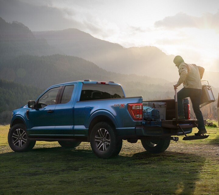 Man using the tailgate step on a 2022 Ford F-150® XL with STX Appearance Package in Atlas Blue at a campground