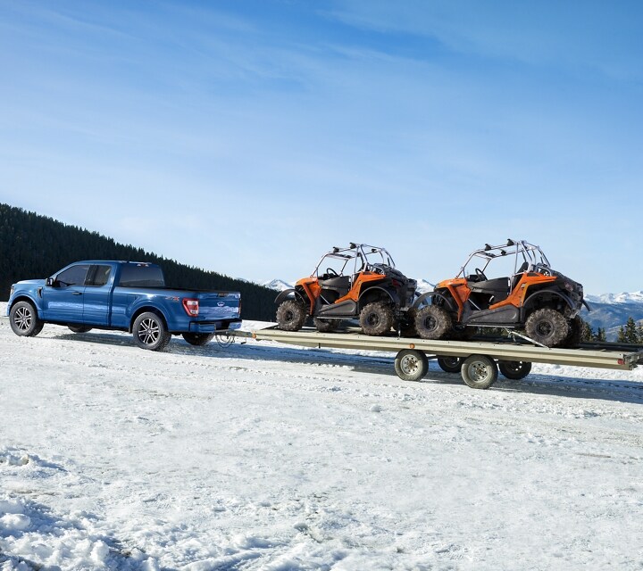 A 2023 Ford F-150® towing two tractor trucks in the snow