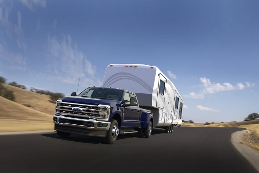 2026 Ford Super Duty® F-250® Lariat® model in Argon Blue driving down a paved highway while towing a large camper.
