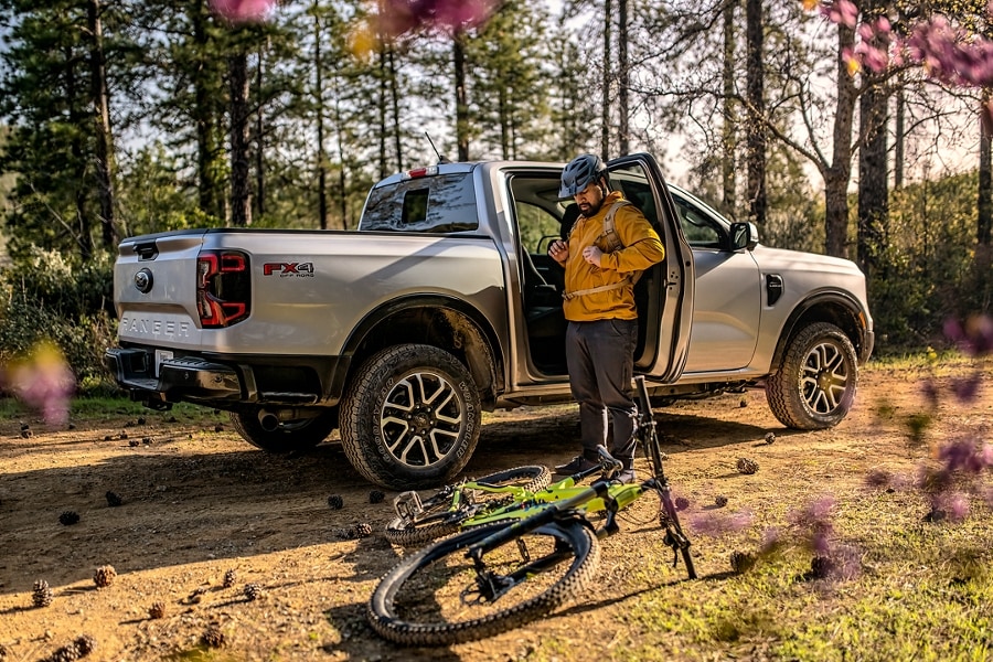 A man stands in the open passenger door of a silver Ford Ranger, with a bicycle on the ground in front.