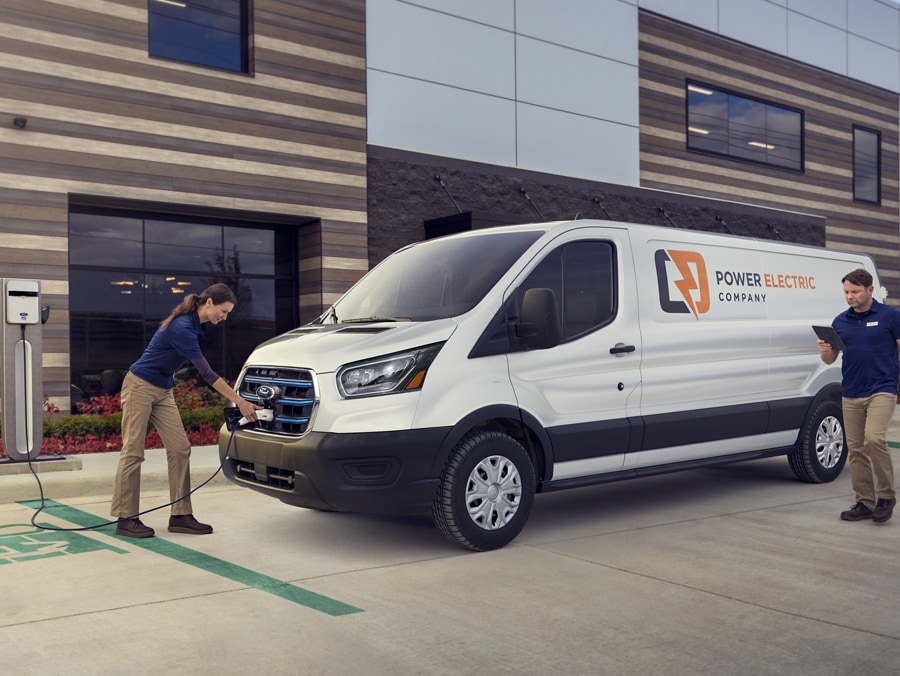 Person charges an E-Transit van in front of a commercial building.
