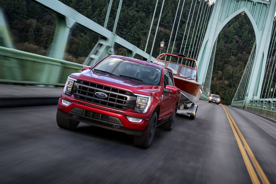 2022 Ford F-150® LARIAT PowerBoost™ Hybrid in Race Red pulling a boat on an expansion bridge