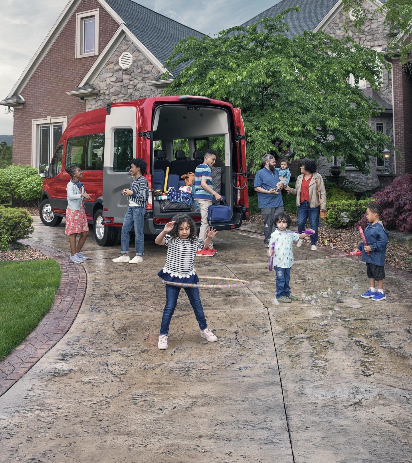 Two parents and a group of children stand behind a red Ford Transit Passenger Van.