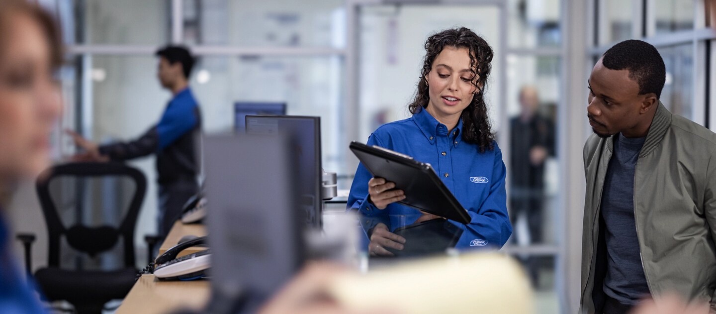 Ford employee holding a tablet speaking with a customer.