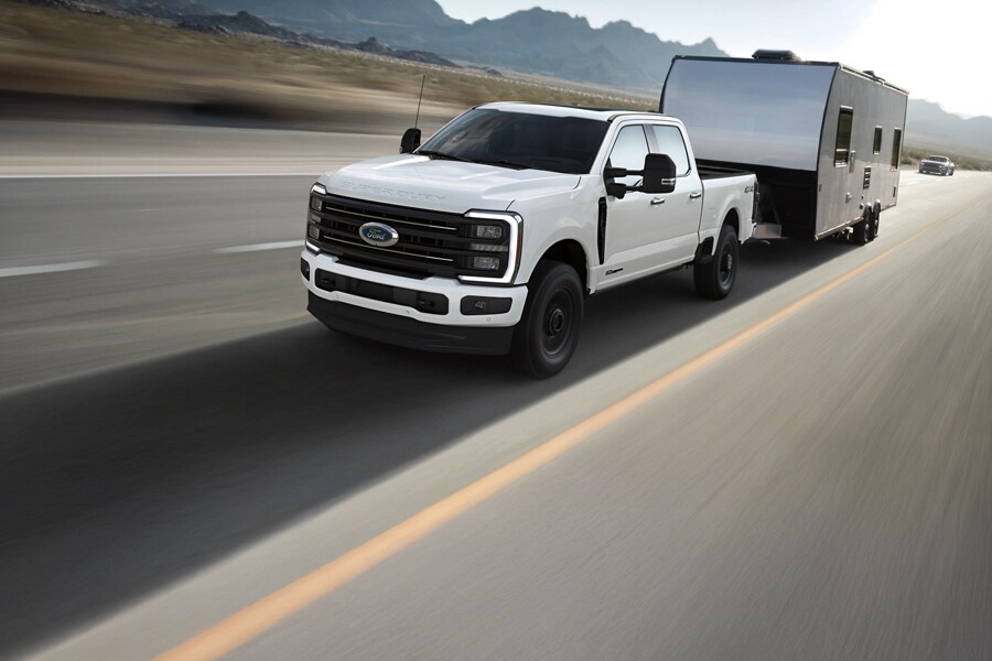 A white ford pulls a camping trailer down a highway.