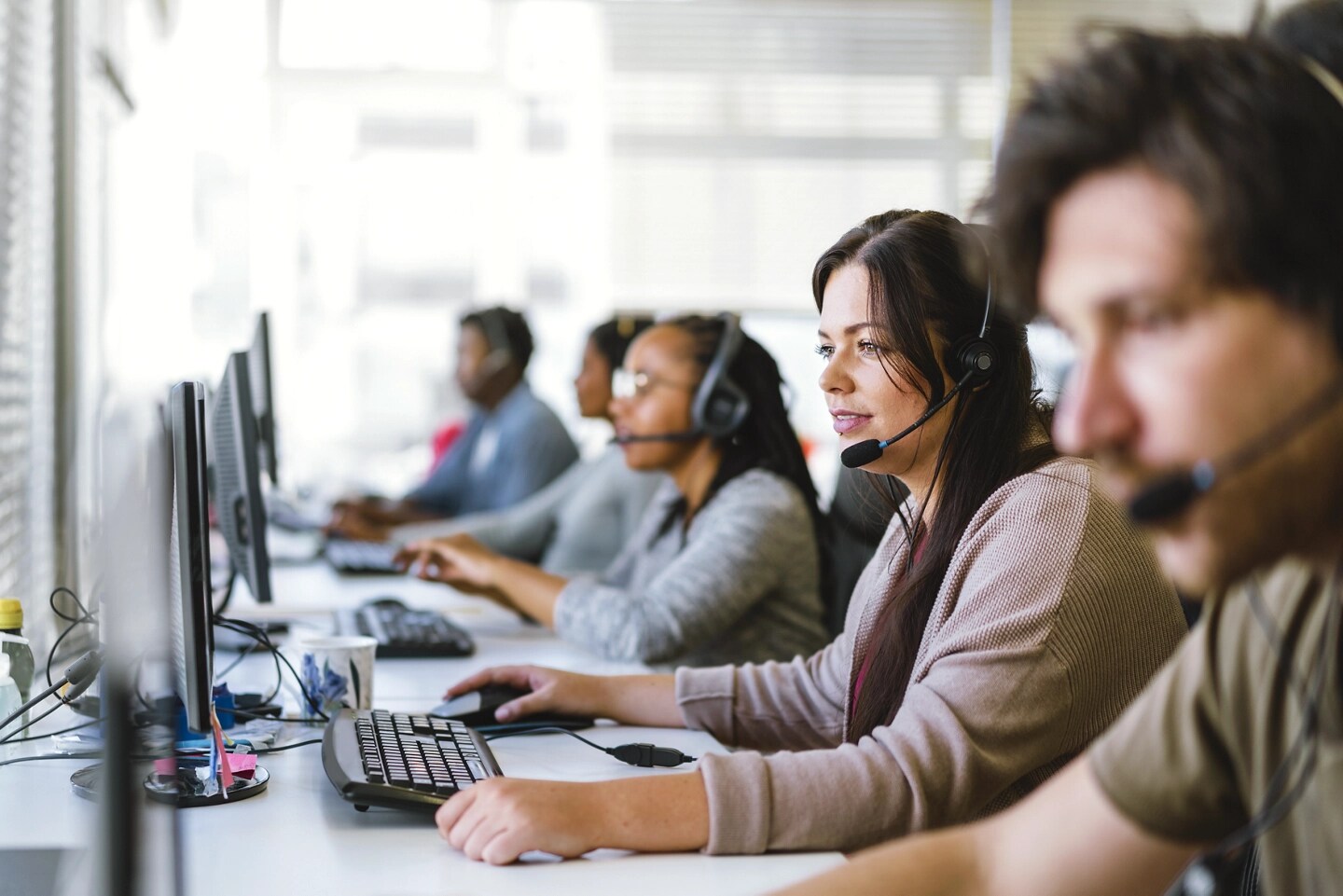 A team of customer service agents, all wearing headsets, seated at a row of computers