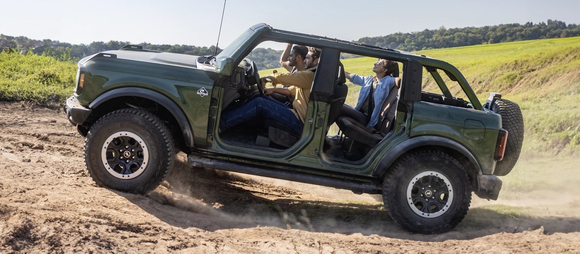 Several people riding on a hilly dirt trail in a 2025 Ford Bronco® SUV with the doors and roof removed