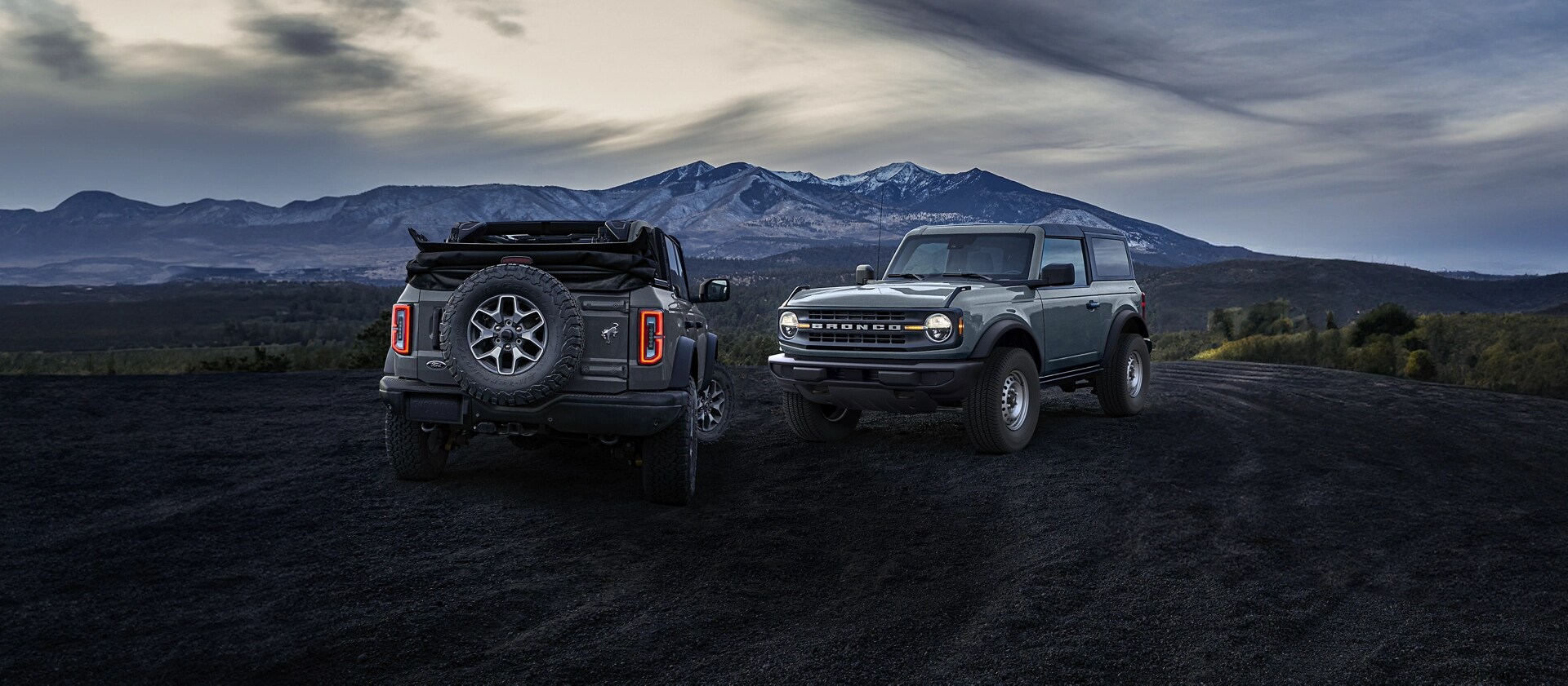Two 2025 Ford Bronco® SUVs parked near a snowcapped mountain, facing opposite directions, illustrating two available roofs