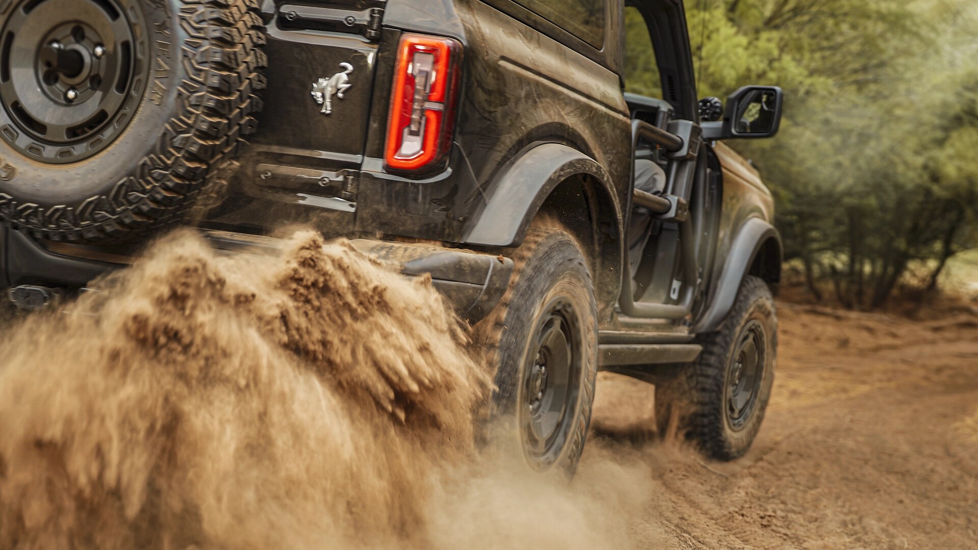 A 2025 Ford Bronco® SUV kicking up mud on a trail in the forest