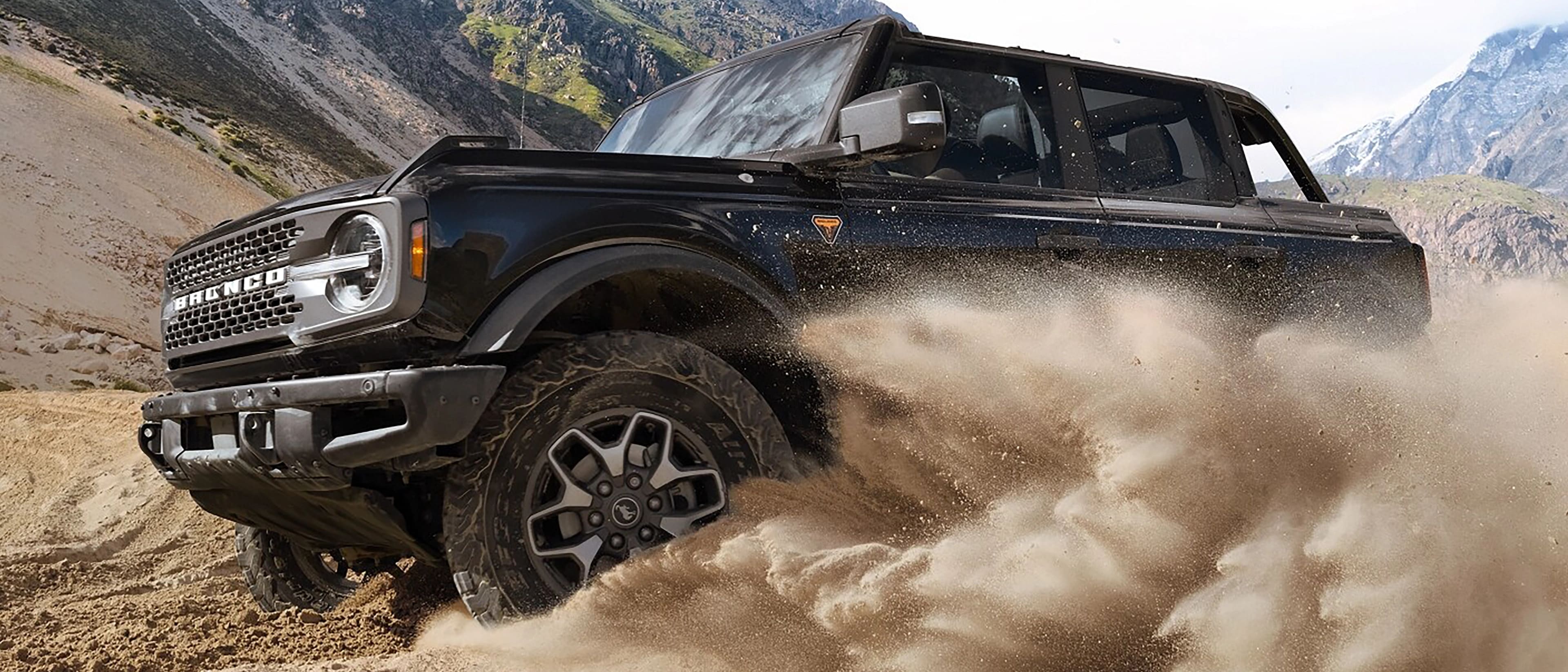 A 2025 Ford Bronco® SUV kicking up sand as it drives in a valley