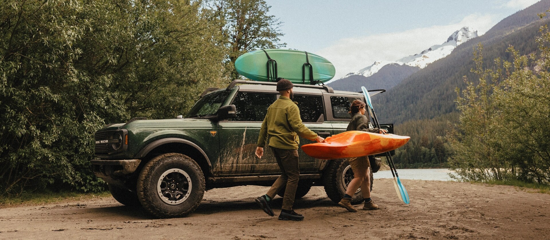 Two people carrying a kayak near a 2025 Ford Bronco® SUV parked near a mountain stream