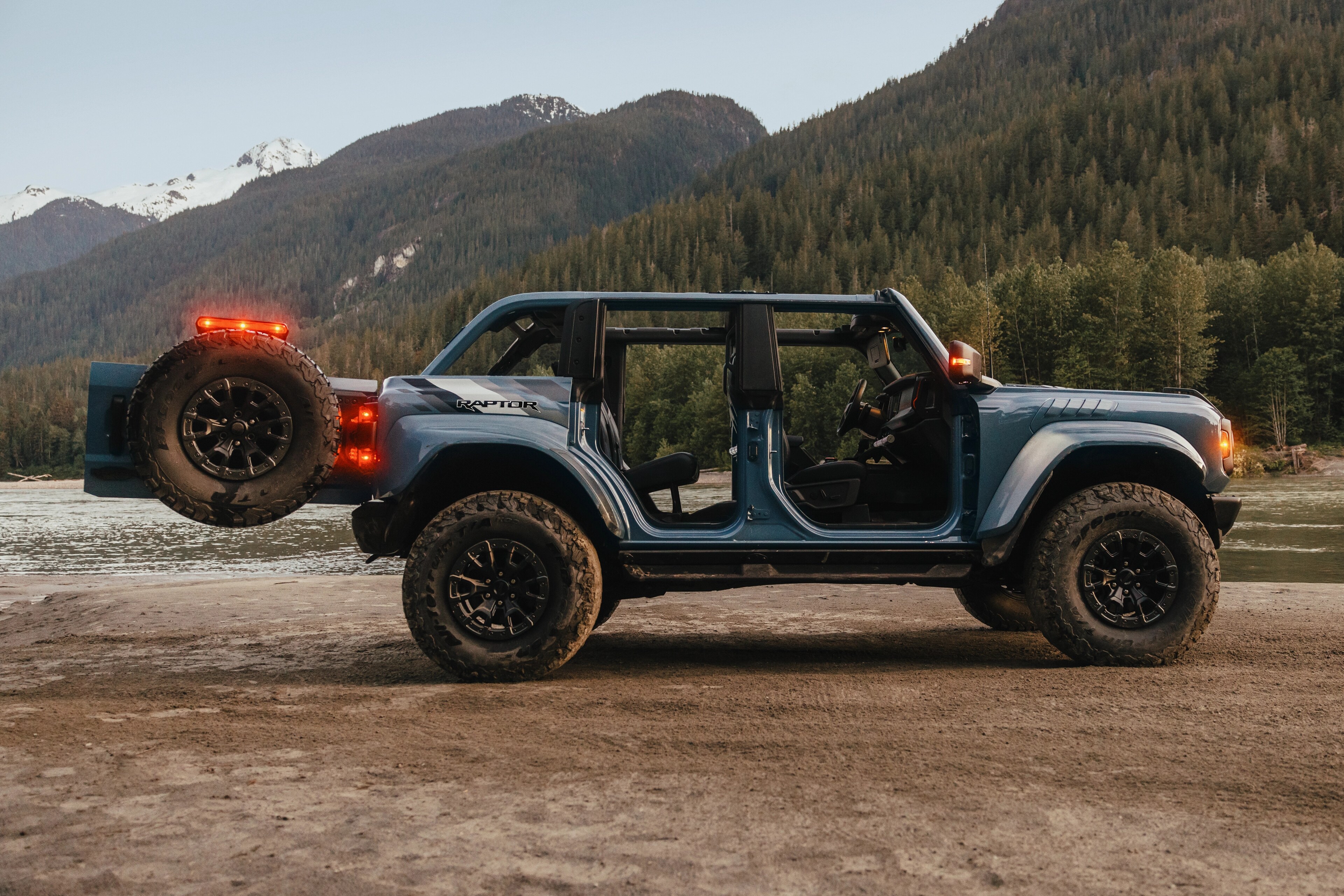 A 2025 Ford Bronco® SUV parked on a mud flat near a mountain lake, with the doors removed and the tailgate open