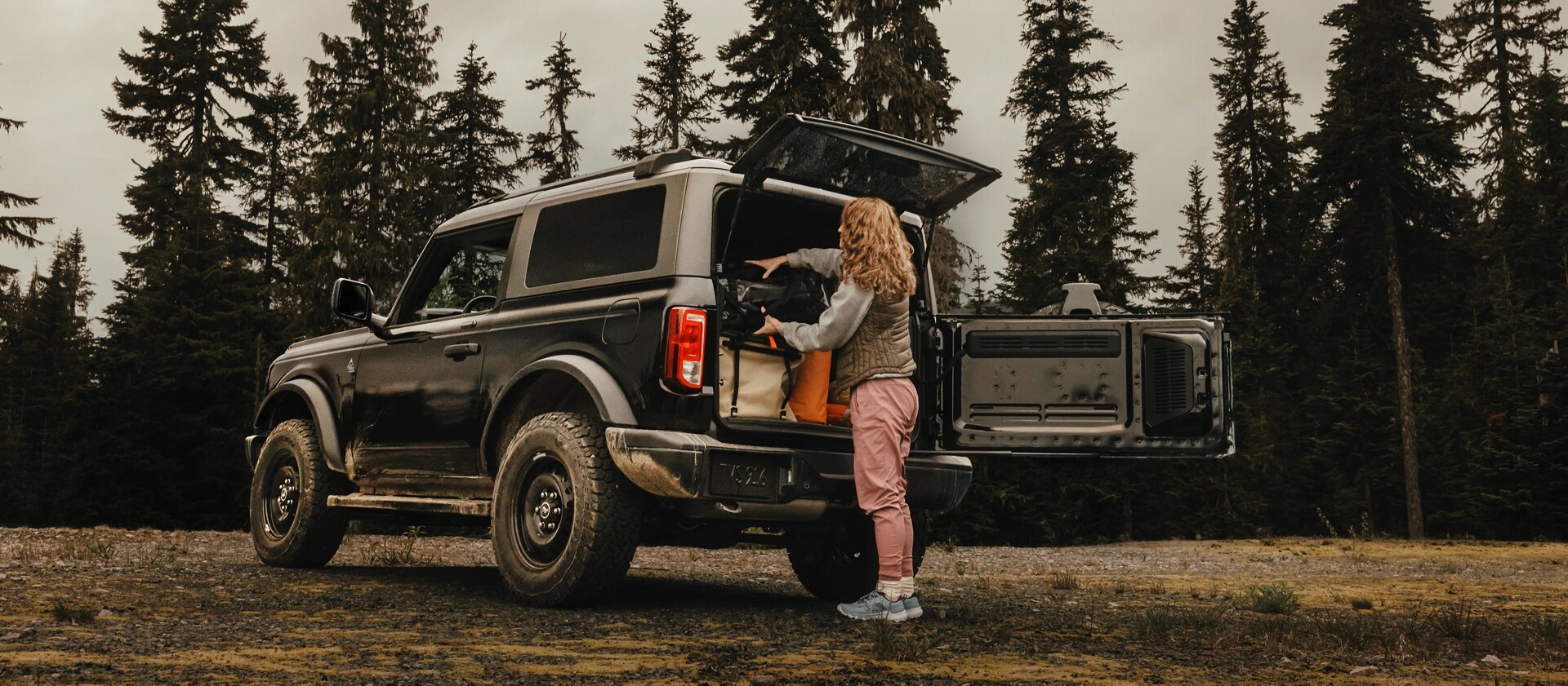 A woman unloading gear from the back of a 2025 Ford Bronco® SUV, showing the side-opening tailgate