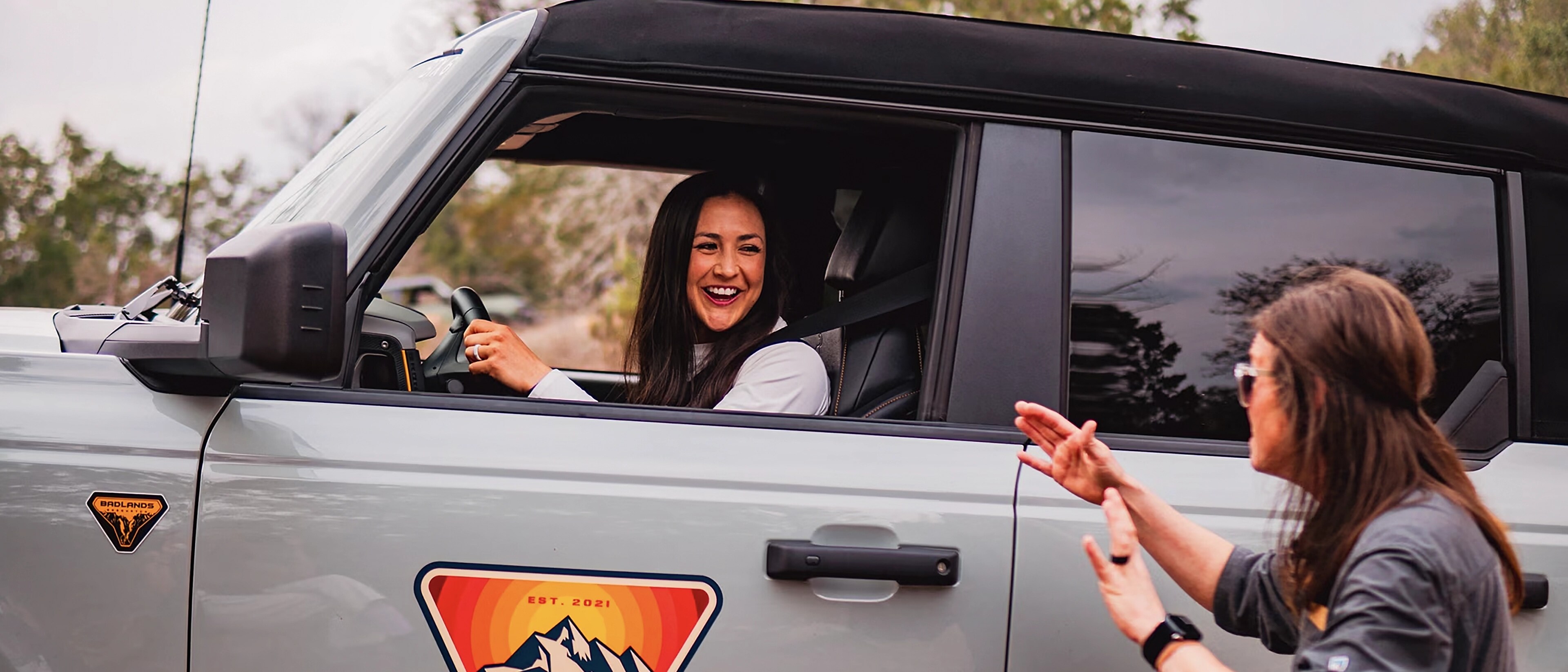 A woman driving a 2025 Ford Bronco® SUV at a Bronco Off-Roadeo® Experience, as an instructor directs from outside the vehicle