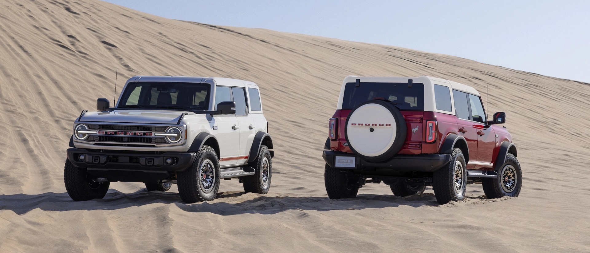 Two 2026 Ford Bronco® SUVs with the available 60th Anniversary Package parked on a sand dune on a sunny morning