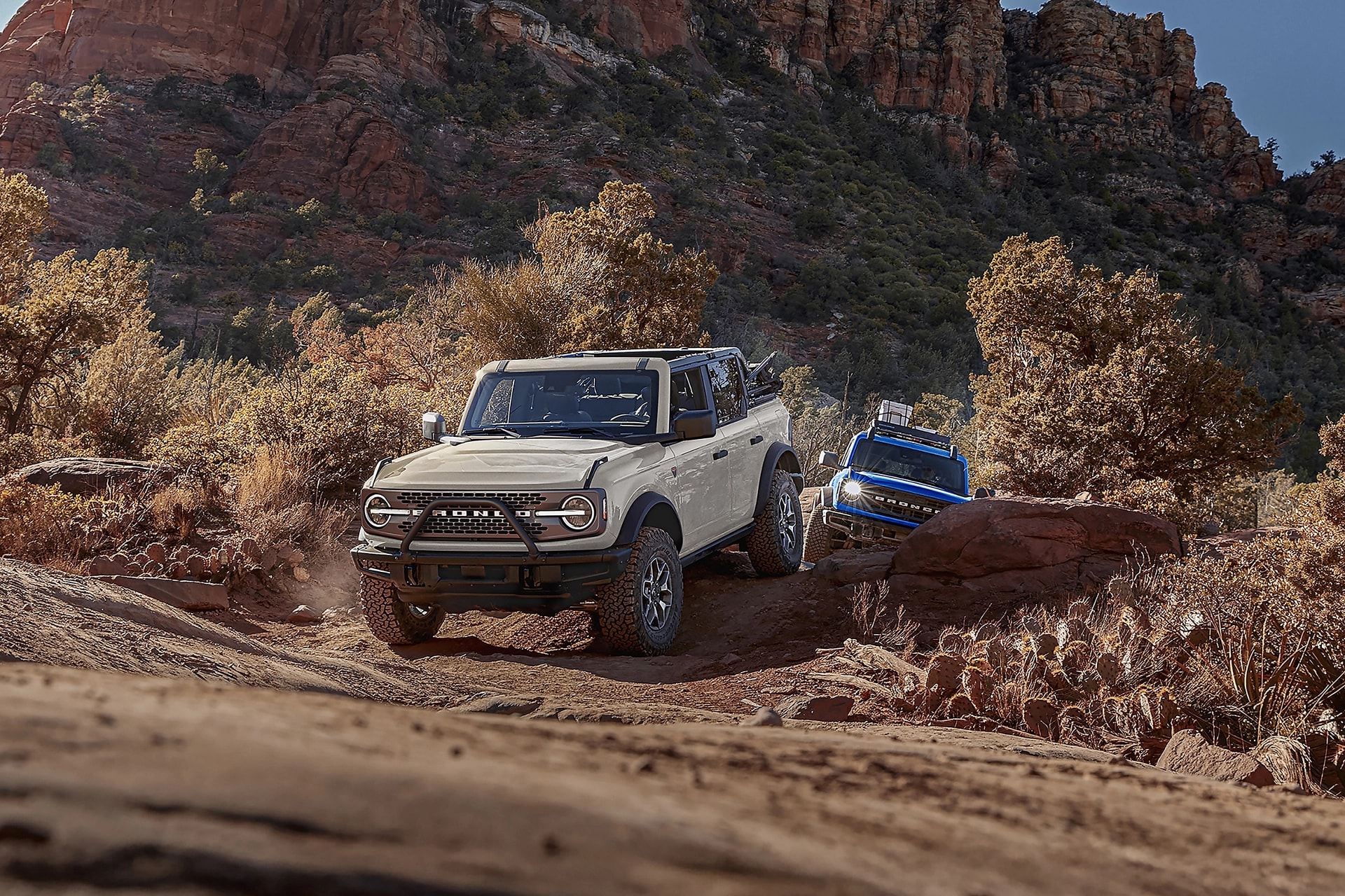 Two 2026 Ford Bronco® SUVs being driven on a scrubby dirt trail