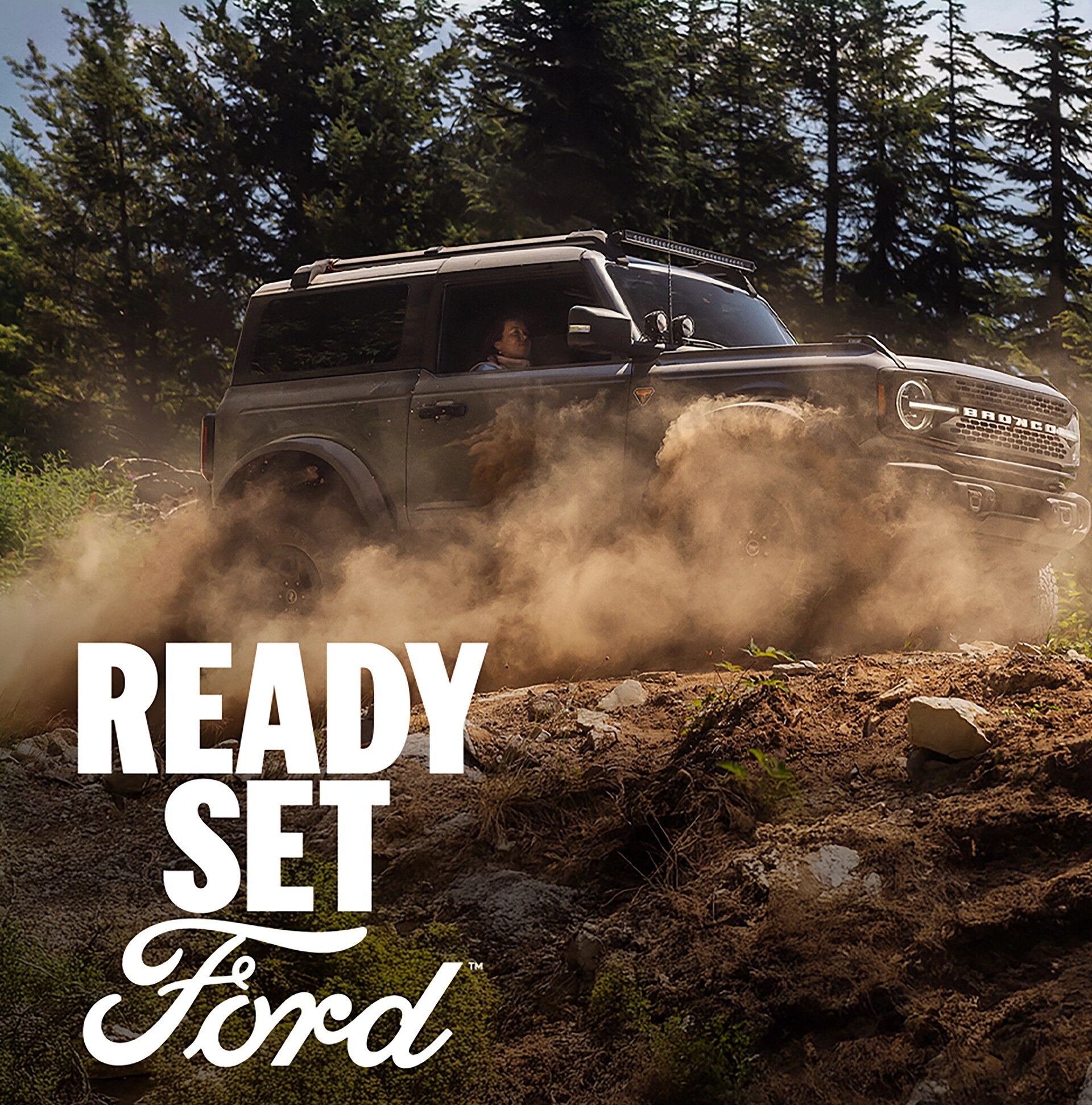 A 2026 Ford Bronco® SUV being driven on a muddy forest trail, with the legend “Ready Set Ford” superimposed