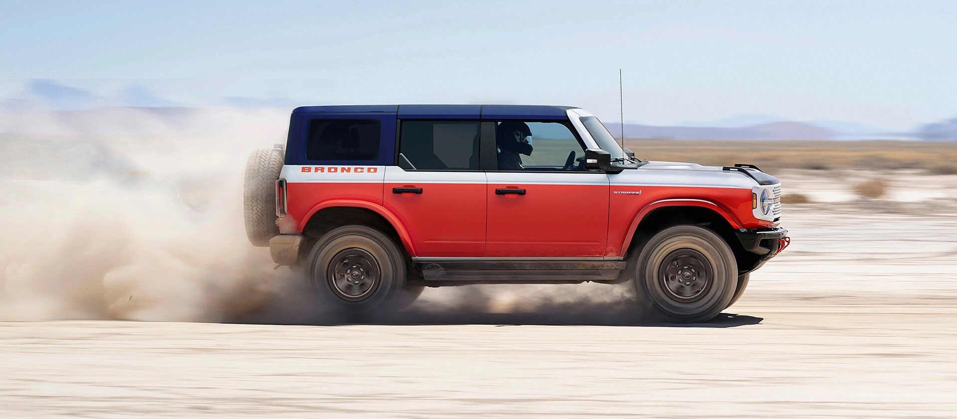 A 2026 Ford Bronco® Stroppe Edition SUV kicking up sand on a salt pan in the desert