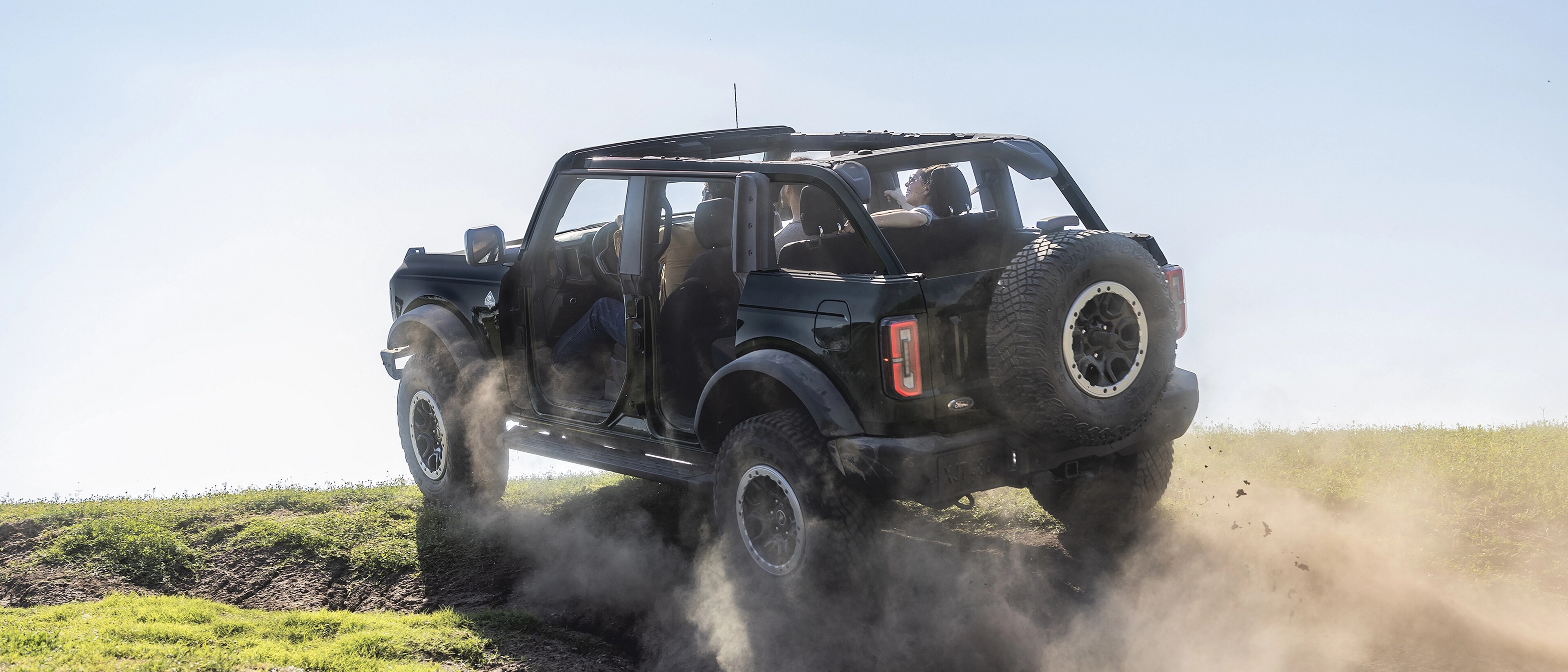 A 2026 Ford Bronco® SUV with the doors removed being driven up a dusty knoll