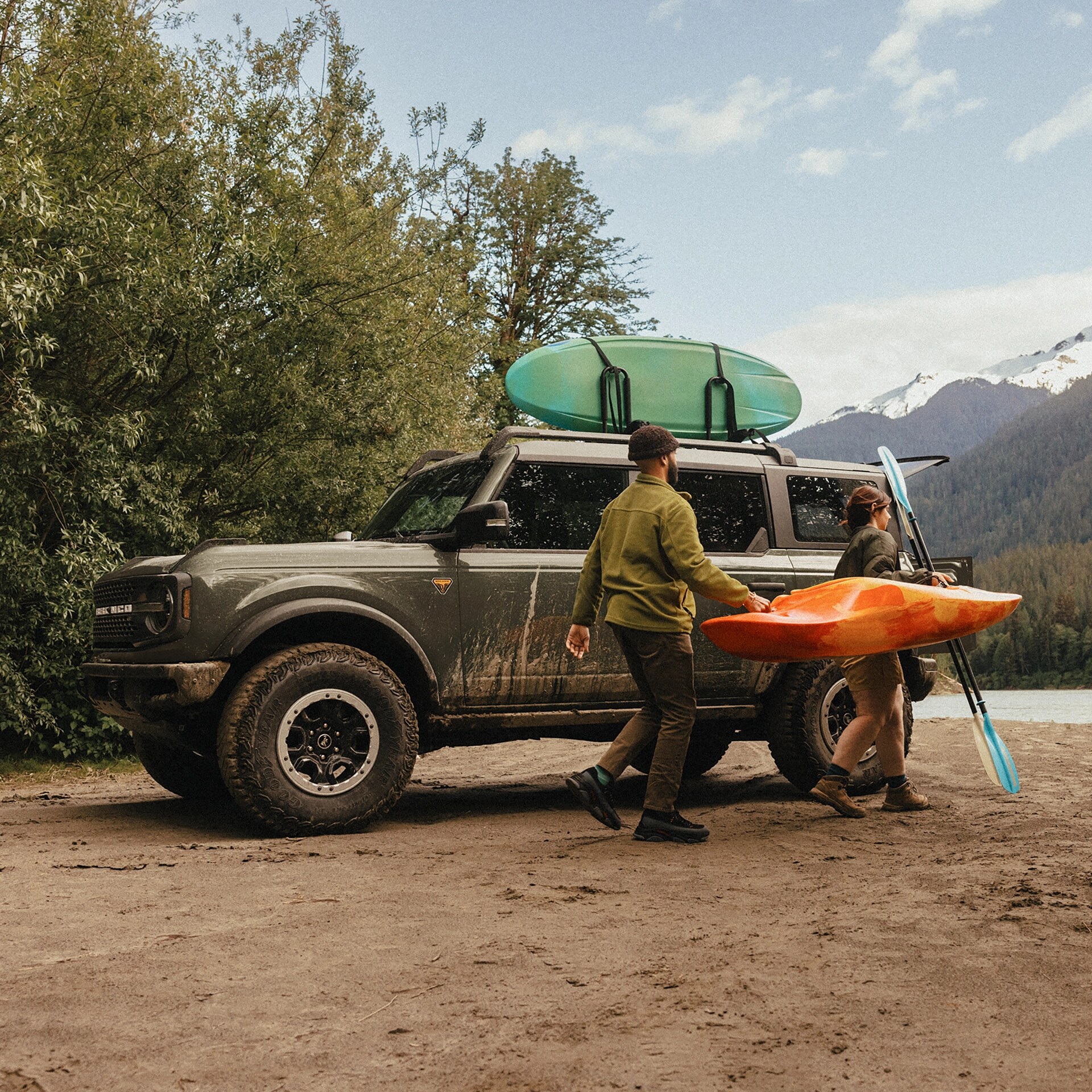 A man and woman carrying a kayak and paddle away from a 2026 Ford Bronco® SUV parked on a mud flat