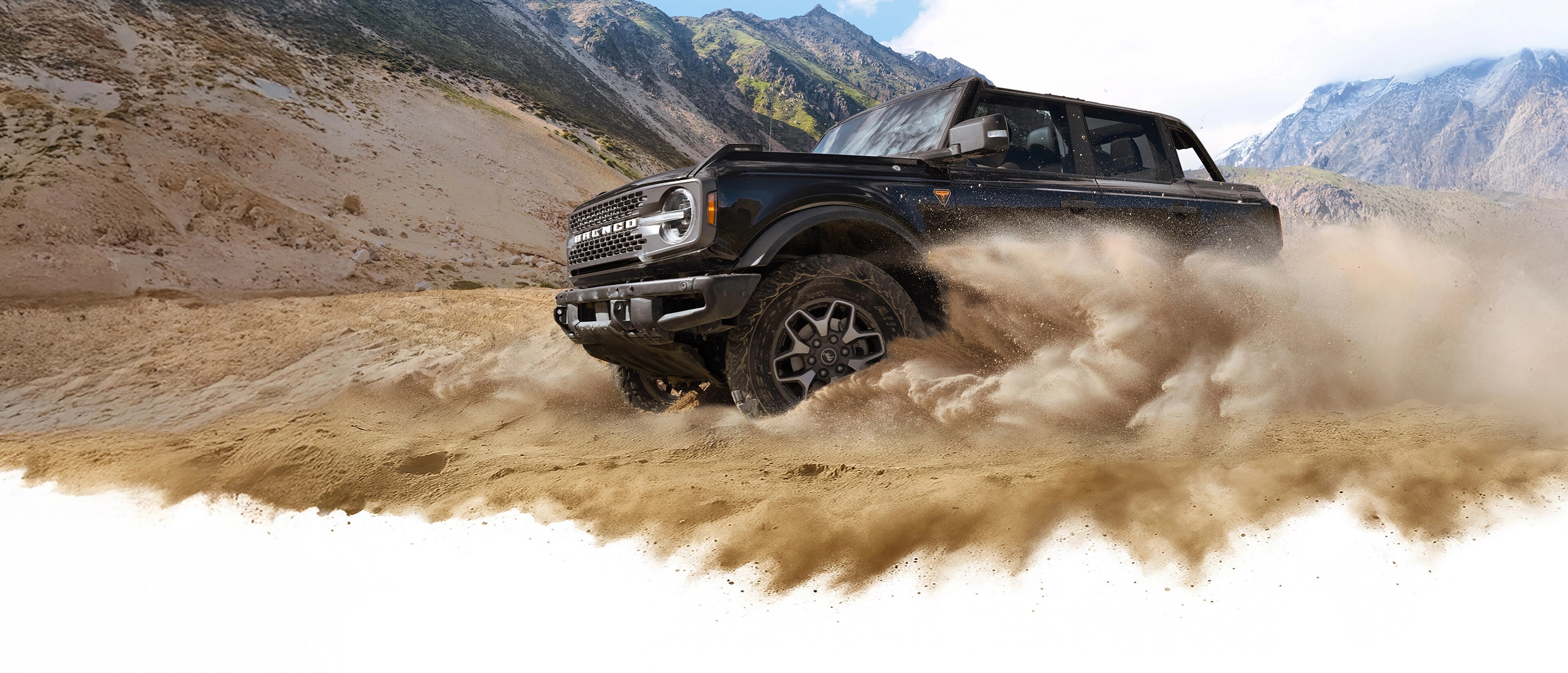 A 2026 Ford Bronco® SUV kicking up dust in a valley beneath rocky hills