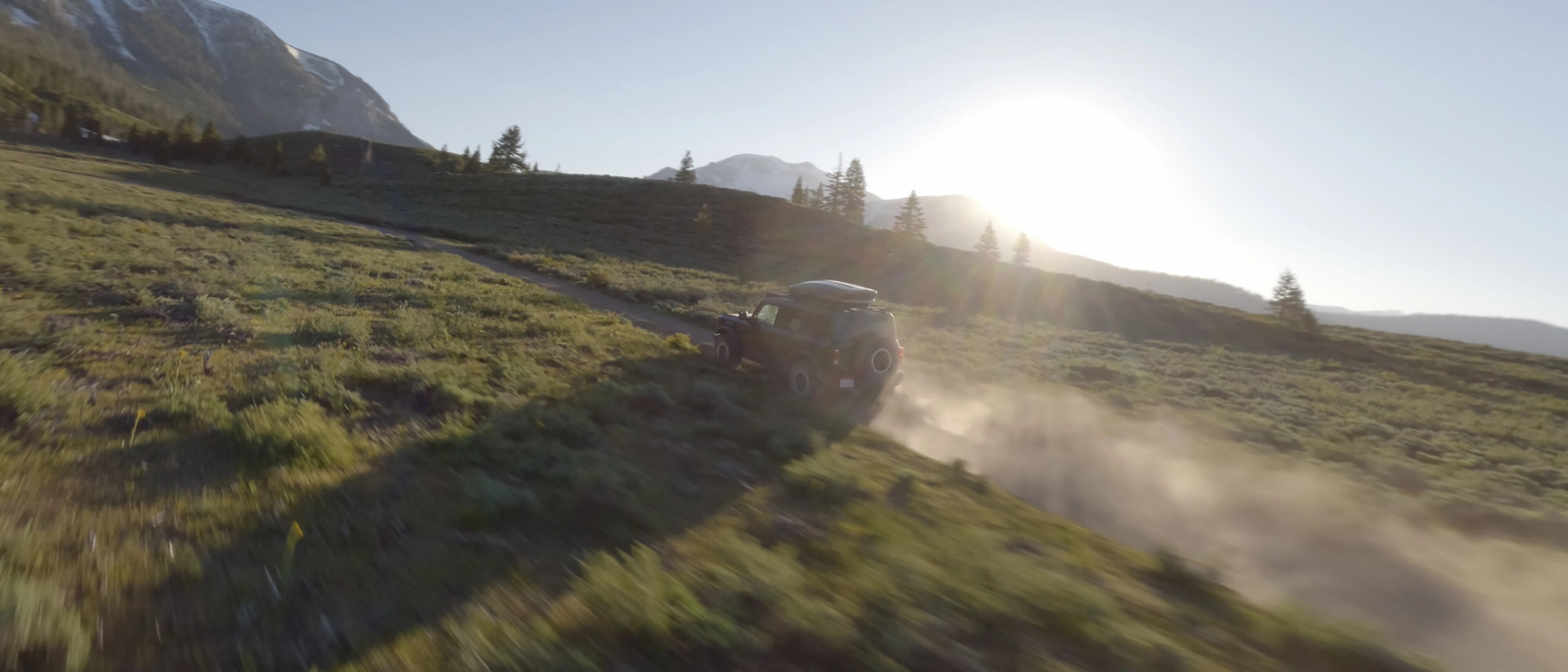 A 2026 Ford Bronco® SUV kicking up dust as it's driven through a grassy valley